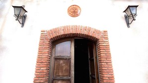 A traditional arched doorway with a wooden door, flanked by two wall-mounted lanterns and a decorative sun emblem above.