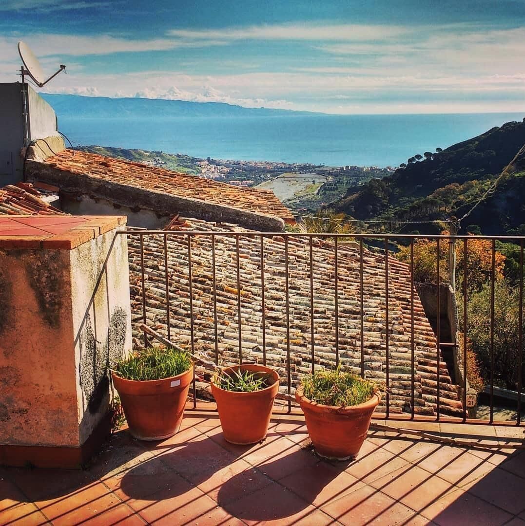 A terrace with terracotta tiles, a metal railing, and three terracotta pots with plants.