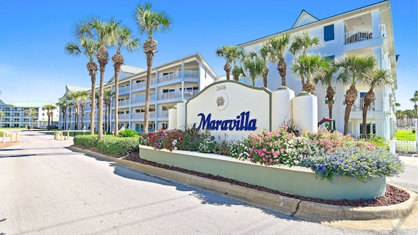 A hotel with a sign reading 'Maravilla,' surrounded by palm trees and a flower bed.