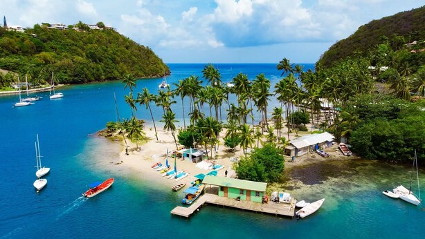 Una isla tropical con un muelle, barcos y un pequeño edificio.