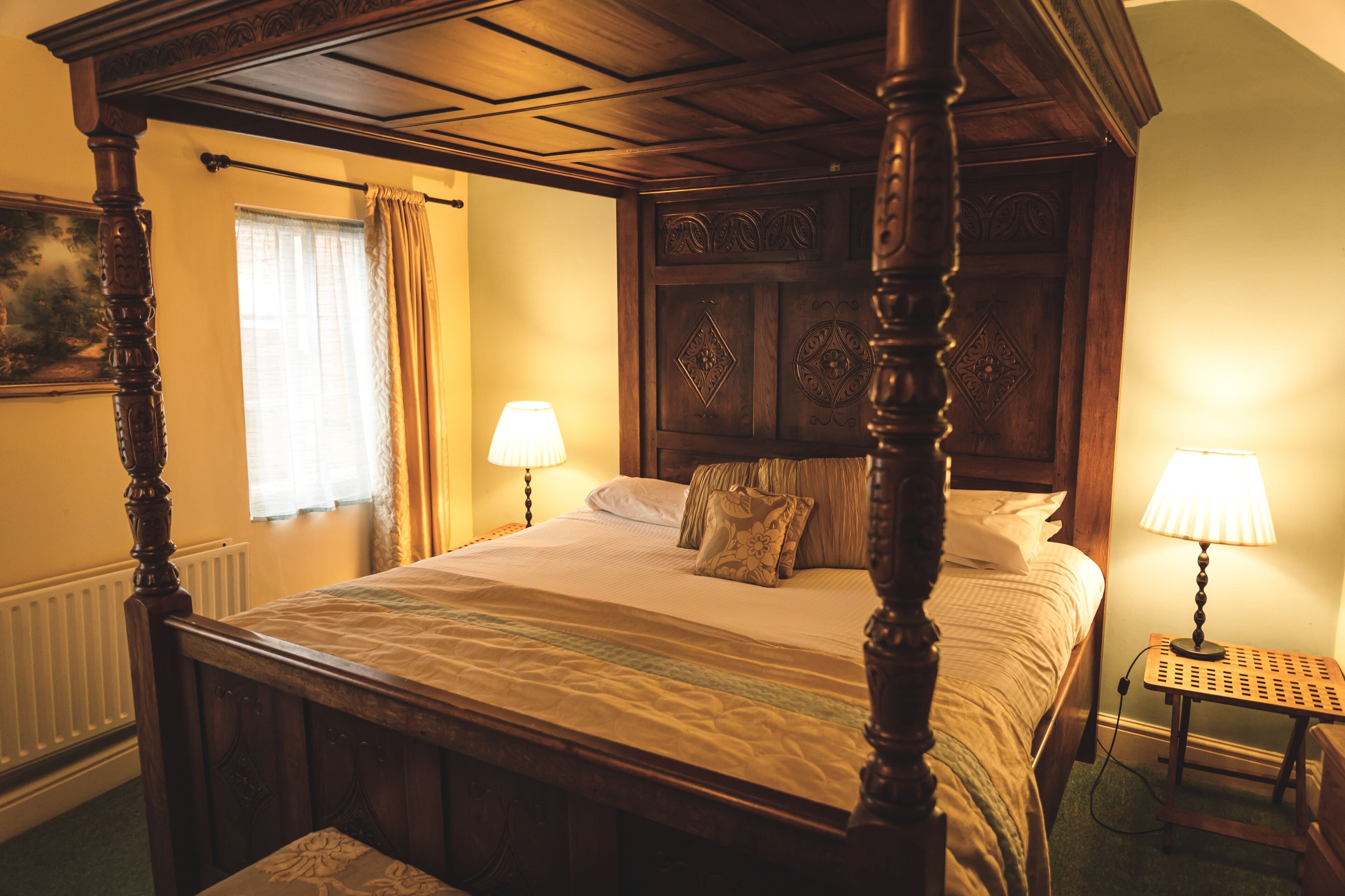 A four-poster bed with a wooden headboard, two bedside lamps, and a nightstand with a lamp.