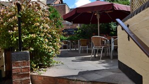 An outdoor patio area with brick steps, wicker chairs, and a red umbrella. - Cromwell's Tap House (Shrewsbury)