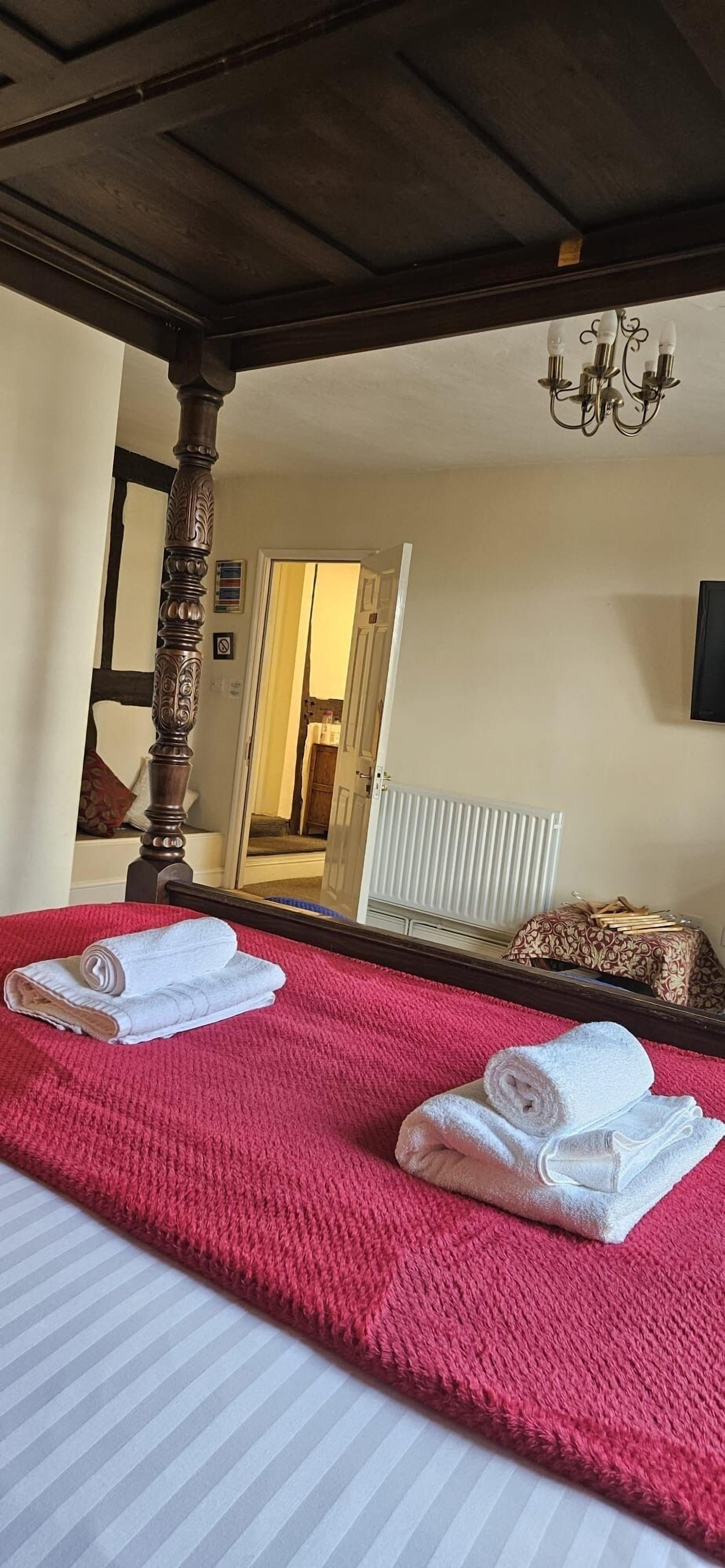 A hotel room with a large bed, a wooden headboard, a chandelier, and a mirror reflecting the room.