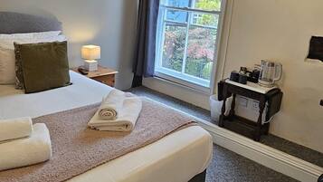 A bedroom with a large bed, a chandelier, a window with a view of buildings, a small table with a coffee maker, and a hanging coat rack.