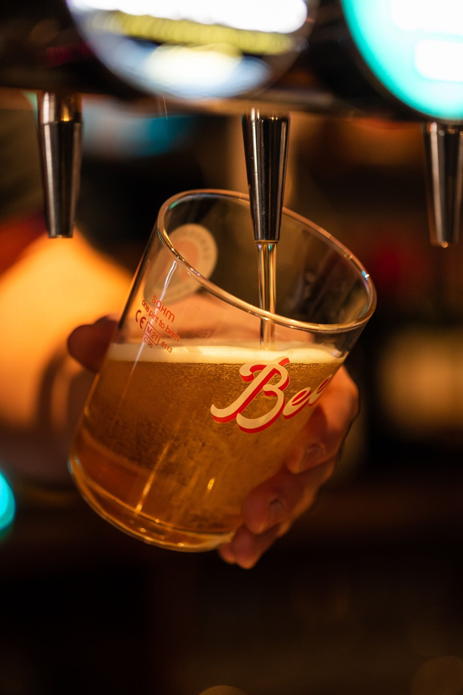 A hand holding a glass of beer with a tap above it.