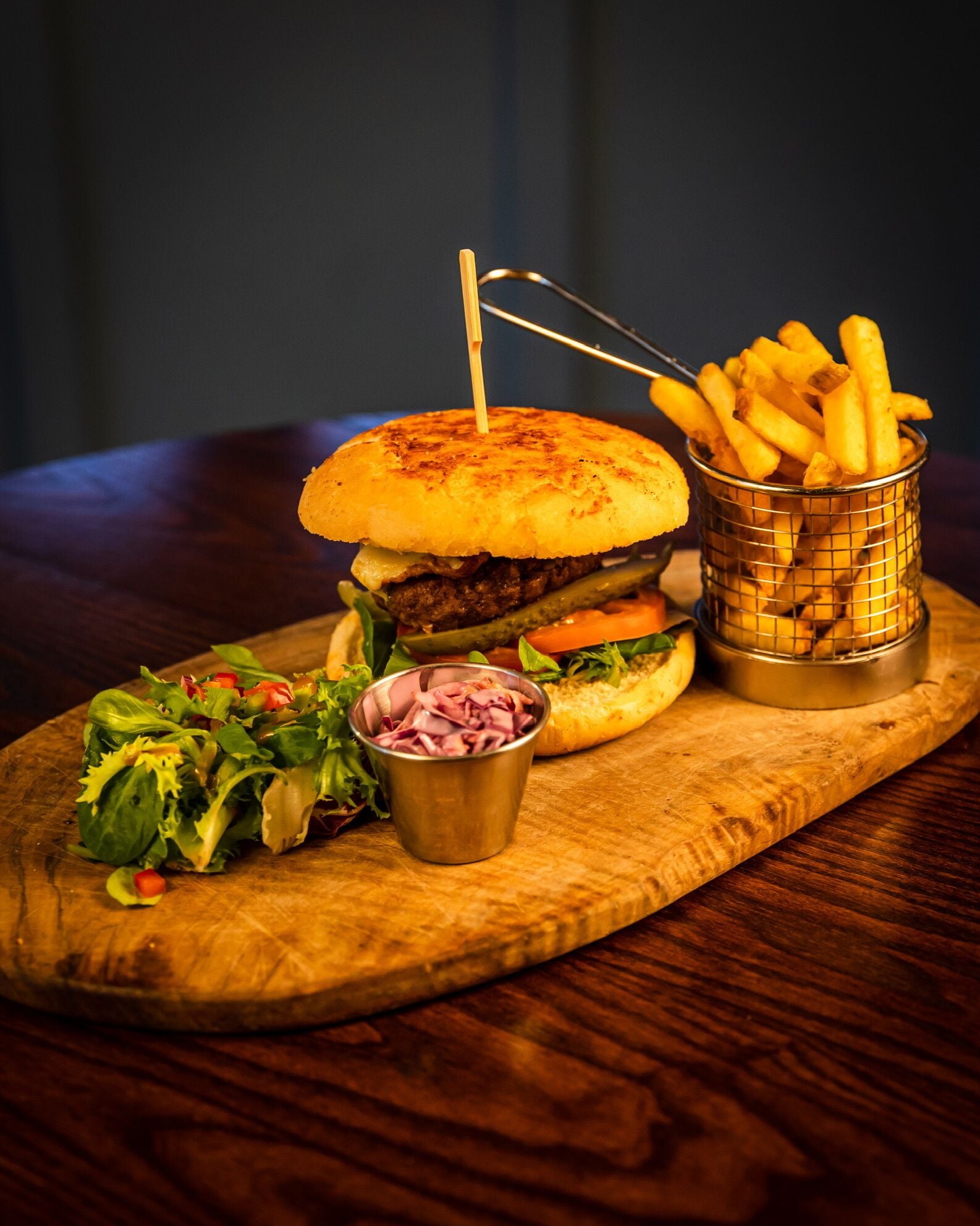 Ein Burger mit Pommes und Salat auf einer Holzplatte.