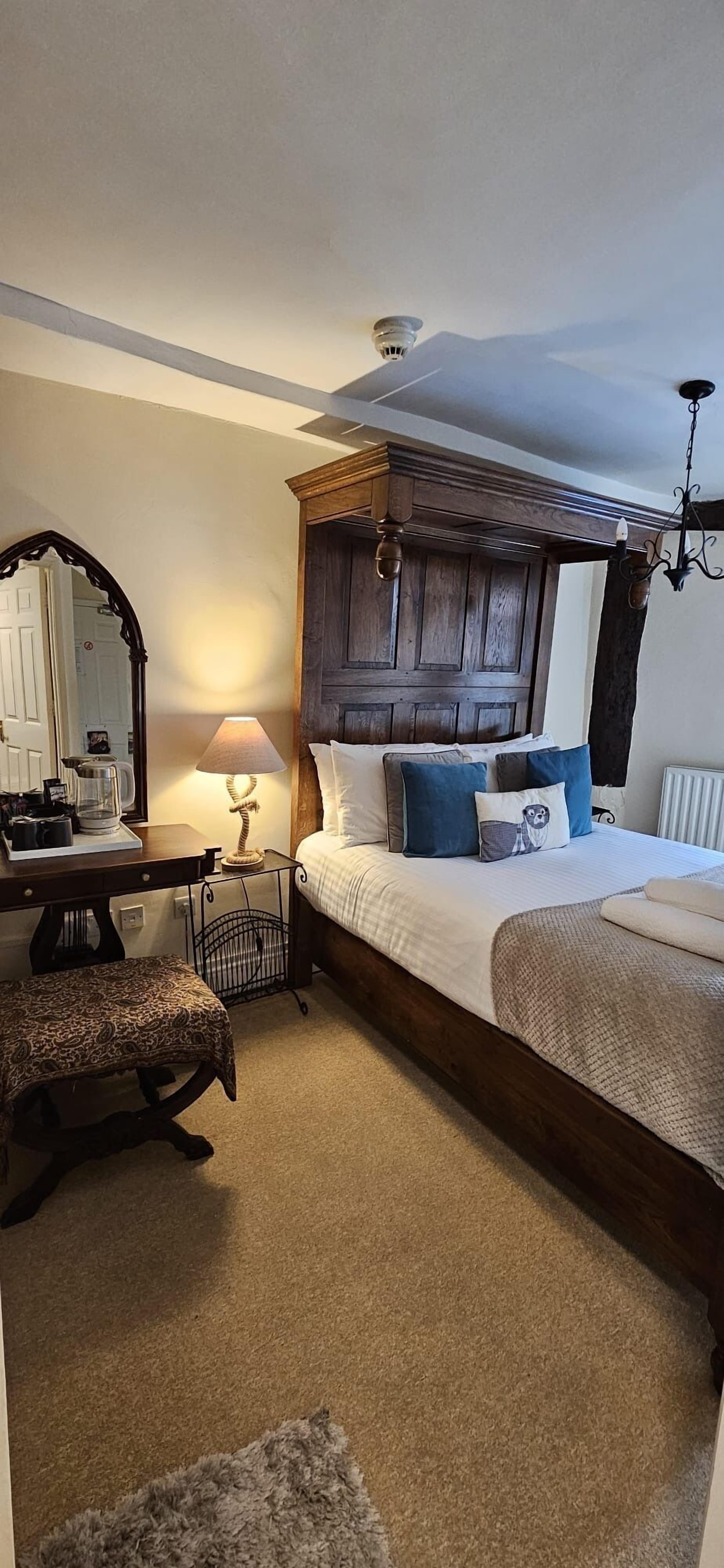 A bedroom with a wooden headboard, a desk with a mirror, a lamp, and a bed with blue and white bedding.