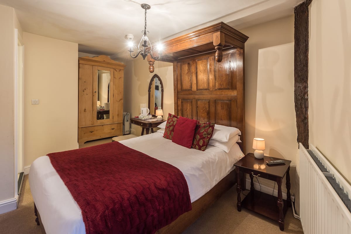 A bedroom with a large bed, wooden wardrobe, and a chandelier.