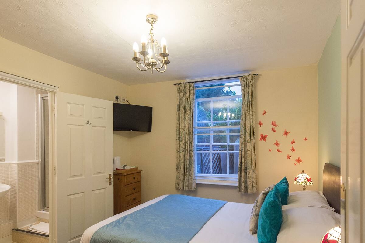 A bedroom with a bed, a dresser, a television mounted on the wall, and a window with curtains.
