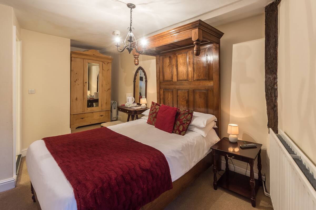 A bedroom with a large bed, wooden wardrobe, and a chandelier.