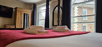 Habitación de hotel con una cama grande, un armario de madera, una televisión y vistas a edificios a través del ventanal.