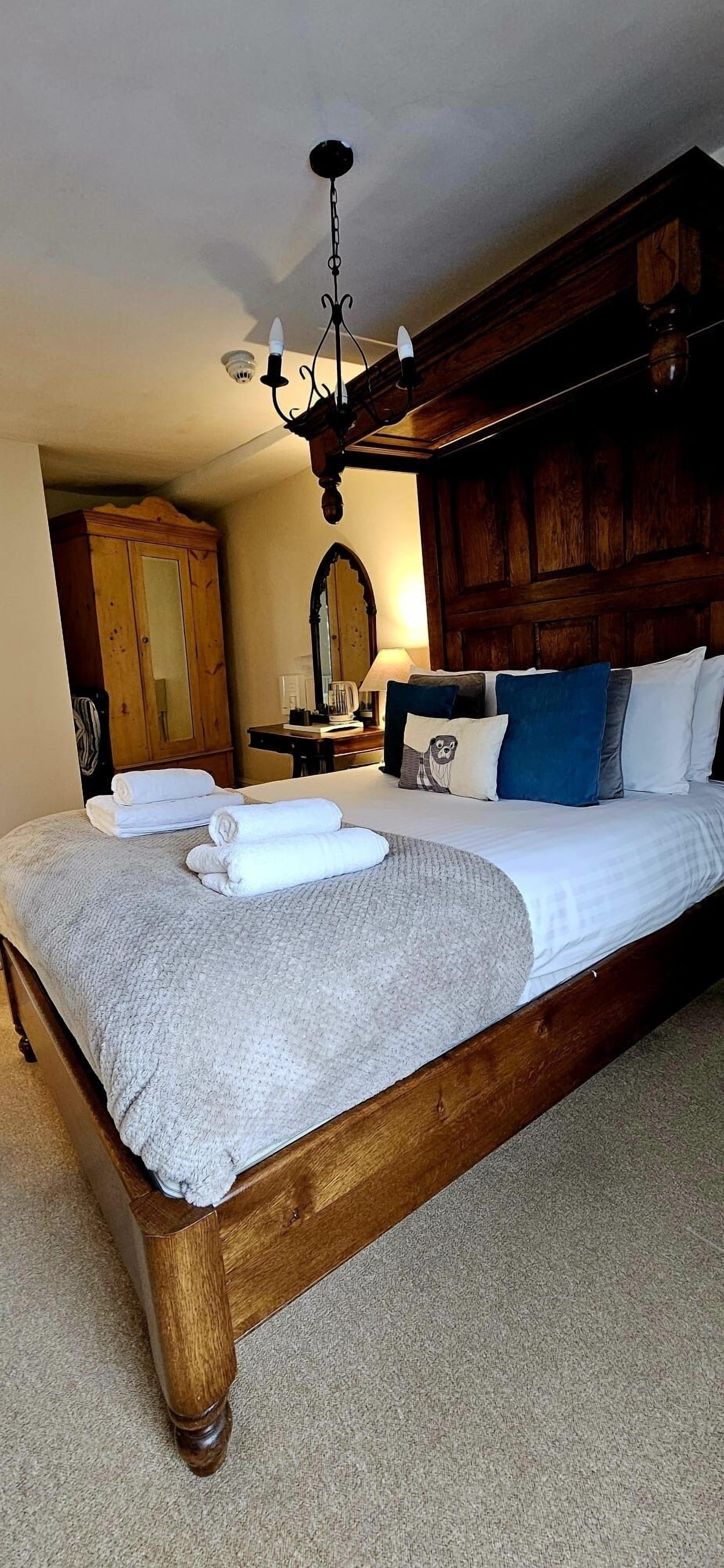A bedroom with a large wooden bed, a chandelier, a wooden wardrobe, and a mirror.