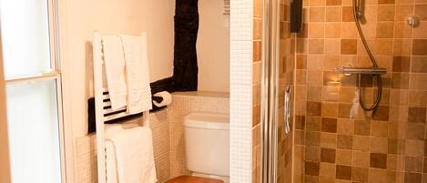 Ein Badezimmer mit Holzboden, Toilette in Weiß, Duschkabine aus Glas und einer Holzbank.