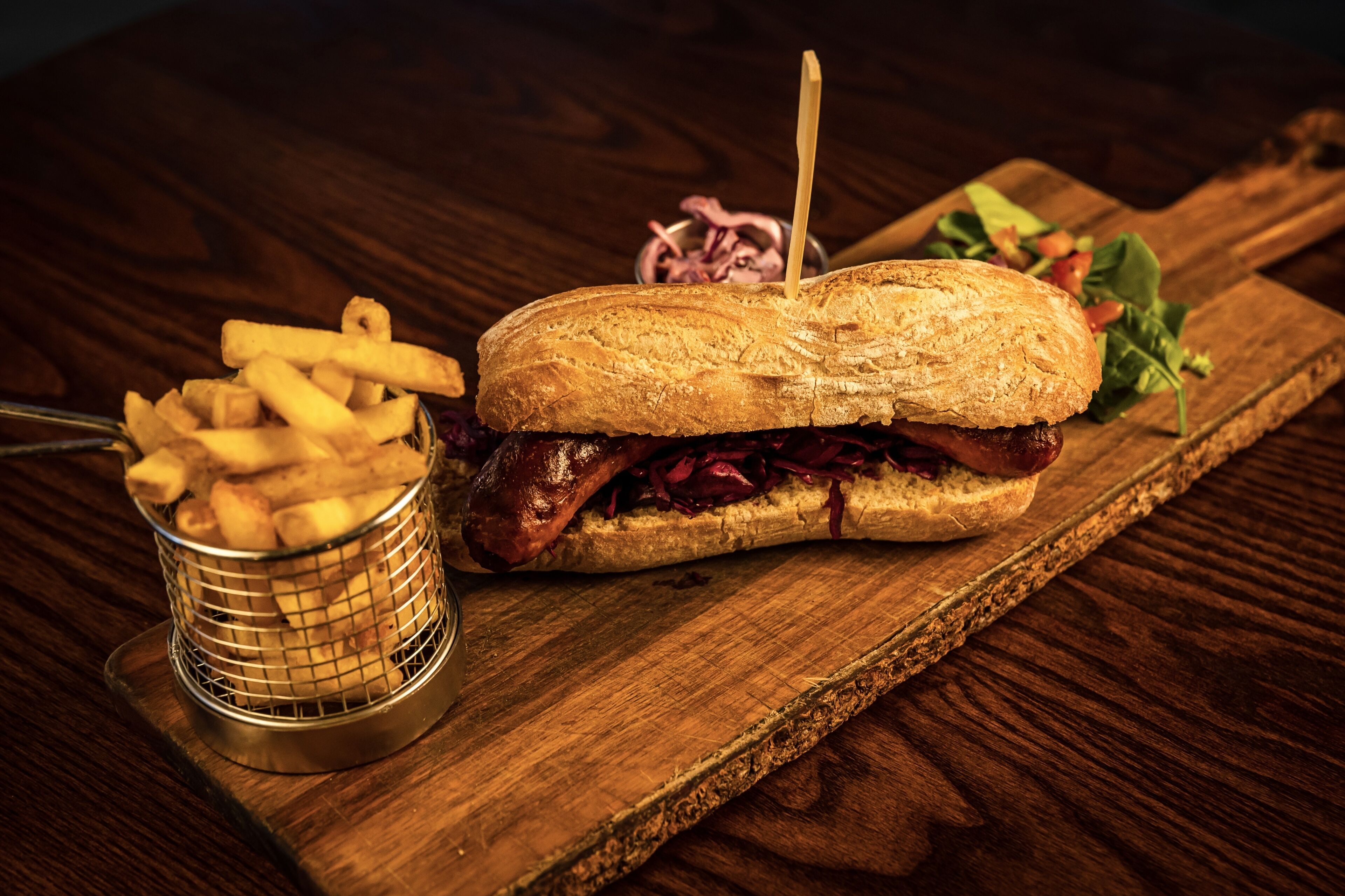 Un sándwich sobre una tabla de madera con papas fritas y una ensalada.