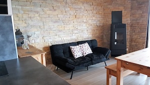 A modern living room with a stone wall, a black sofa, a wooden table, and a fireplace. - Apartment BOUQUETIN in new chalet with view of Lake Matemale sleeps 8 (Les Angles)