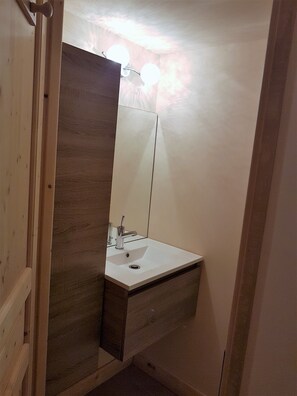 Un baño con tocador de madera, un lavabo blanco y un espejo.