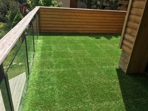 A wooden deck with a glass railing, surrounded by a wooden fence and lush green grass.