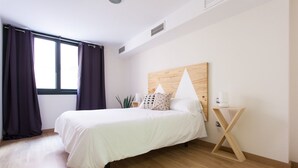 Een slaapkamer met een bed, nachtkastje, houten hoofdbord en een raam met gordijnen.