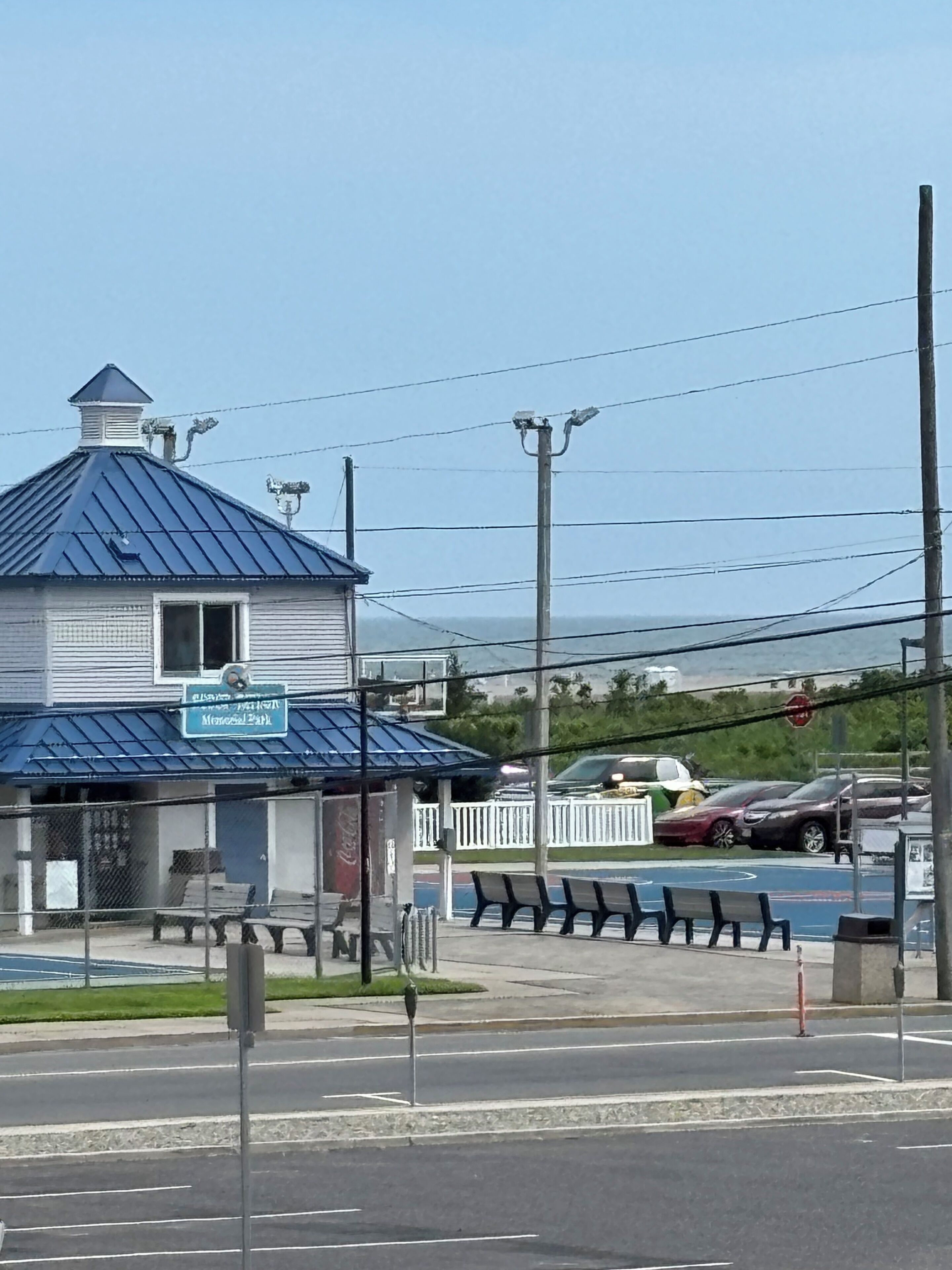 A building with a blue roof and a Coca-Cola sign, located at a street corner with benches and a parking area.