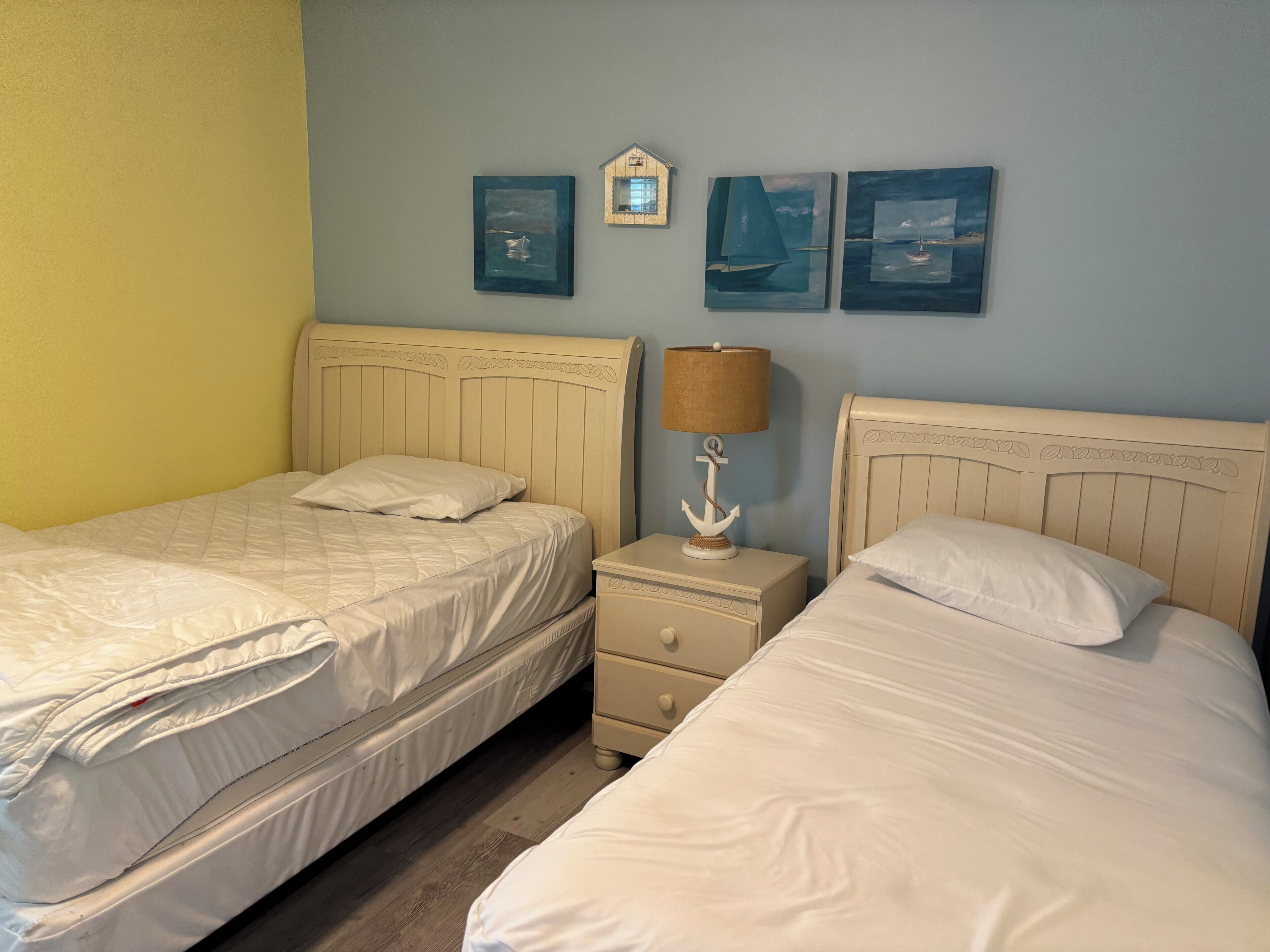 Una habitación con dos camas, una mesita de noche con lámpara y tres cuadros colgados en la pared.
