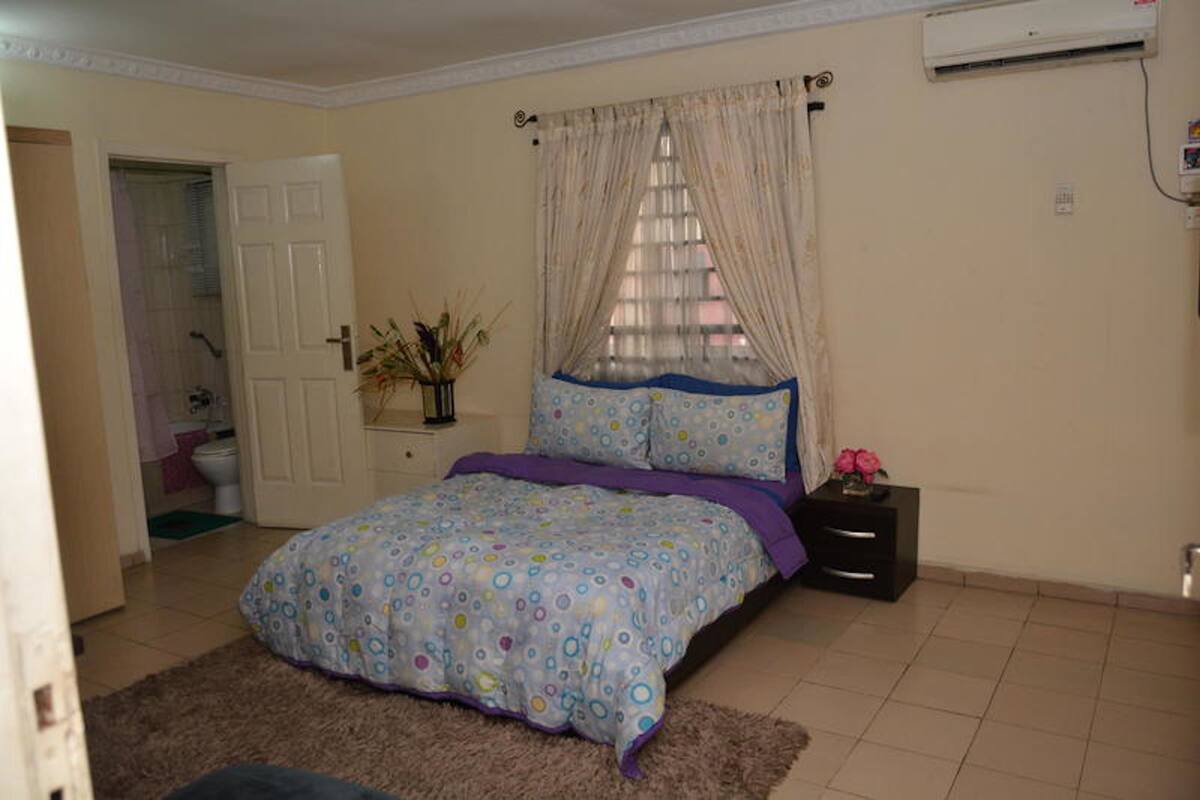 A bedroom with a bed, a nightstand, a vase with flowers, and a window with curtains.