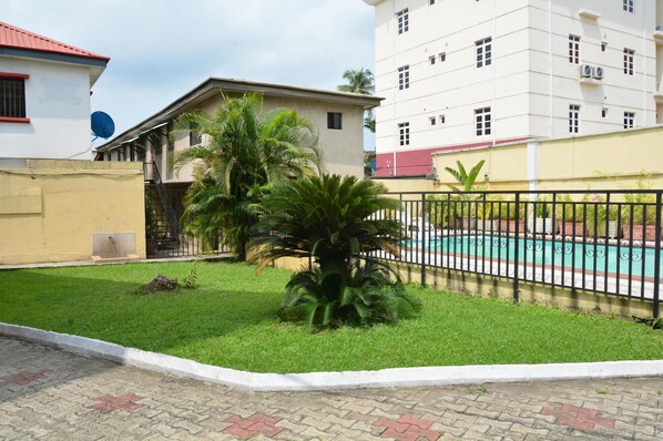 A residential area with a swimming pool, a small garden with palm trees, and a building with a red roof.
