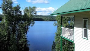 A lakeside cabin with a balcony overlooking a calm lake, surrounded by dense trees. - Birch Haven - A Luxury Lakefront Cottage On Pristine Horsefly Lake, with Wifi (Horsefly)