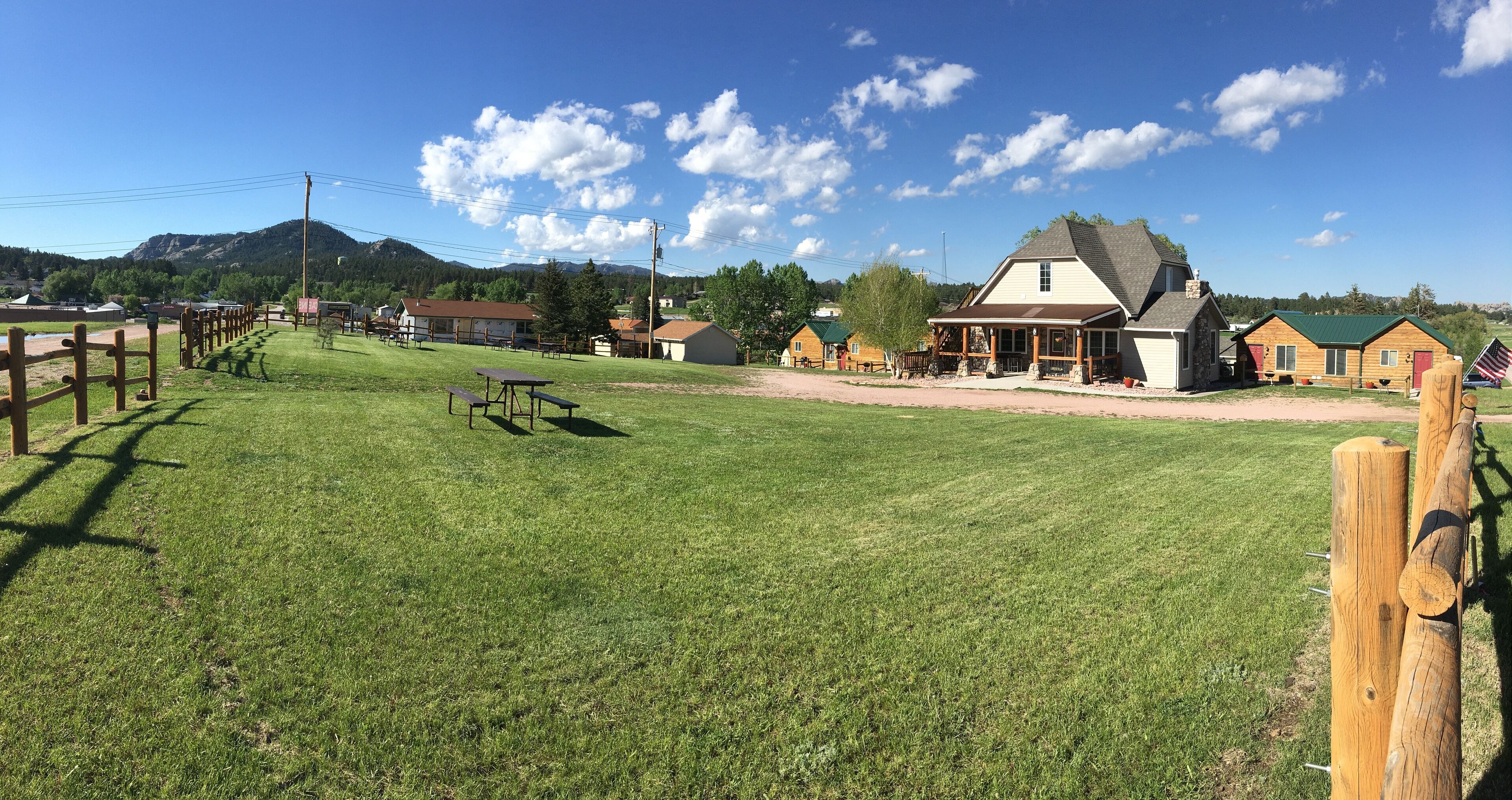 A rural setting with a large grassy field, wooden fences, and a variety of buildings including a prominent house with a porch.