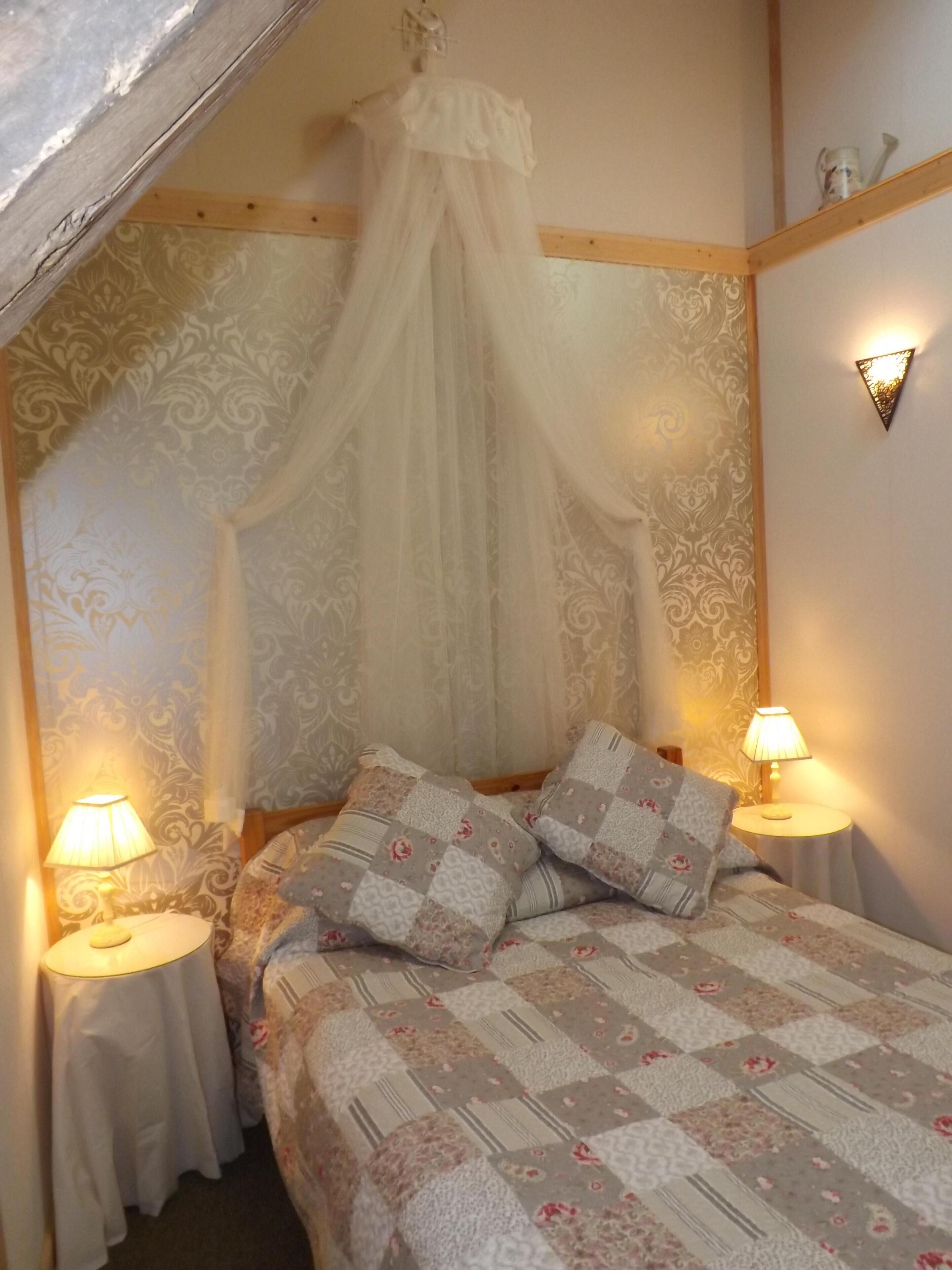 A bedroom with a canopy bed, floral patterned wallpaper, and two bedside lamps.