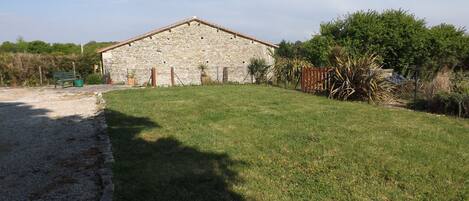 A stone building with a sloped roof, surrounded by a grassy area and a gravel path.