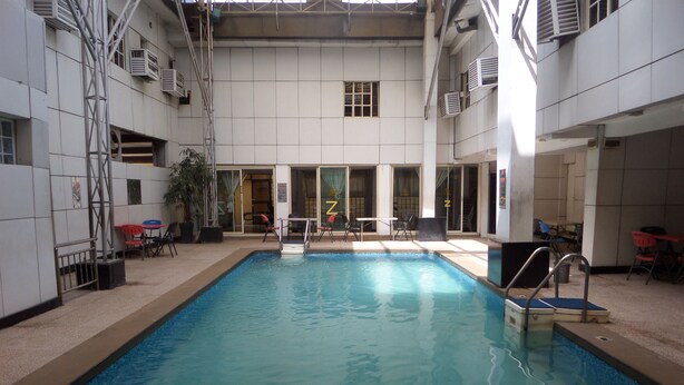 An indoor swimming pool with a tiled floor, surrounded by chairs and tables, and a staircase leading to upper levels. - Zaaz Hotel (Lagos)