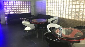 A dimly lit lounge area with a sofa, two round tables, and white chairs. - Zaaz Hotel (Lagos)