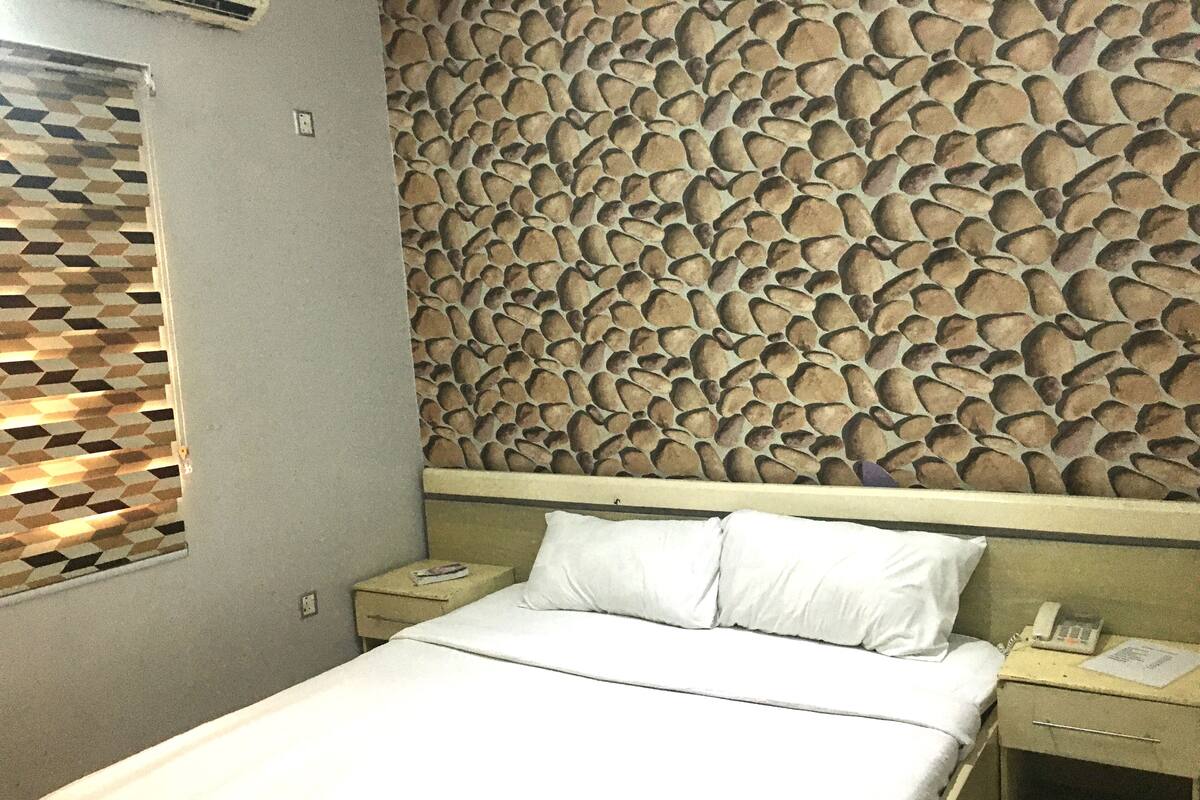 Una habitación de hotel con una cama, una mesita de noche, un teléfono y una pared con textura.