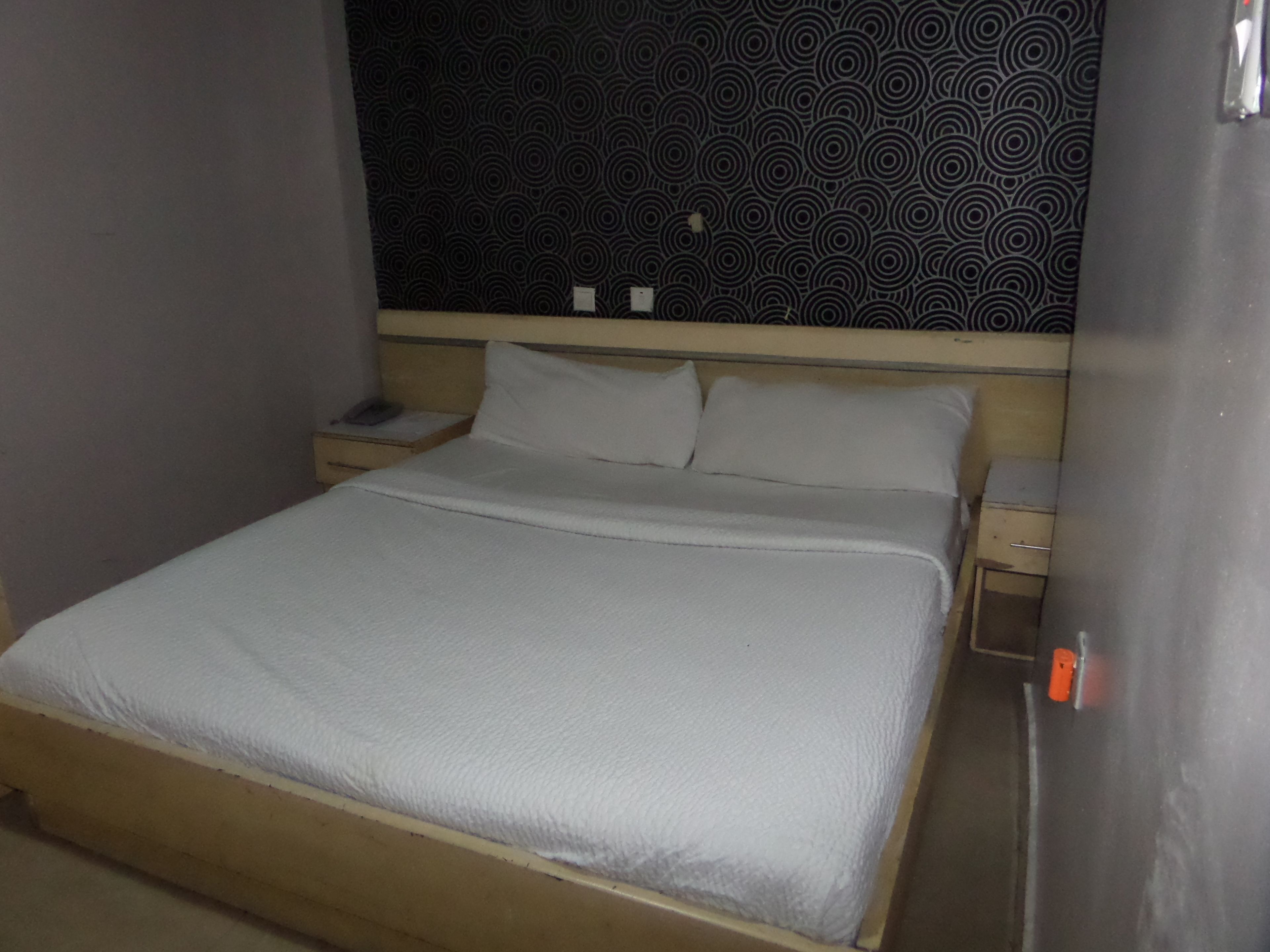 A single bed with a wooden headboard and white bedding in a room with patterned wallpaper.