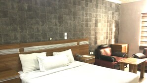 A hotel room with a large bed, a wooden headboard, a desk, and a leather armchair. - Zaaz Hotel (Lagos)