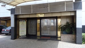 A hotel entrance with a covered walkway, a signboard listing amenities, and a car parked nearby. - Zaaz Hotel (Lagos)