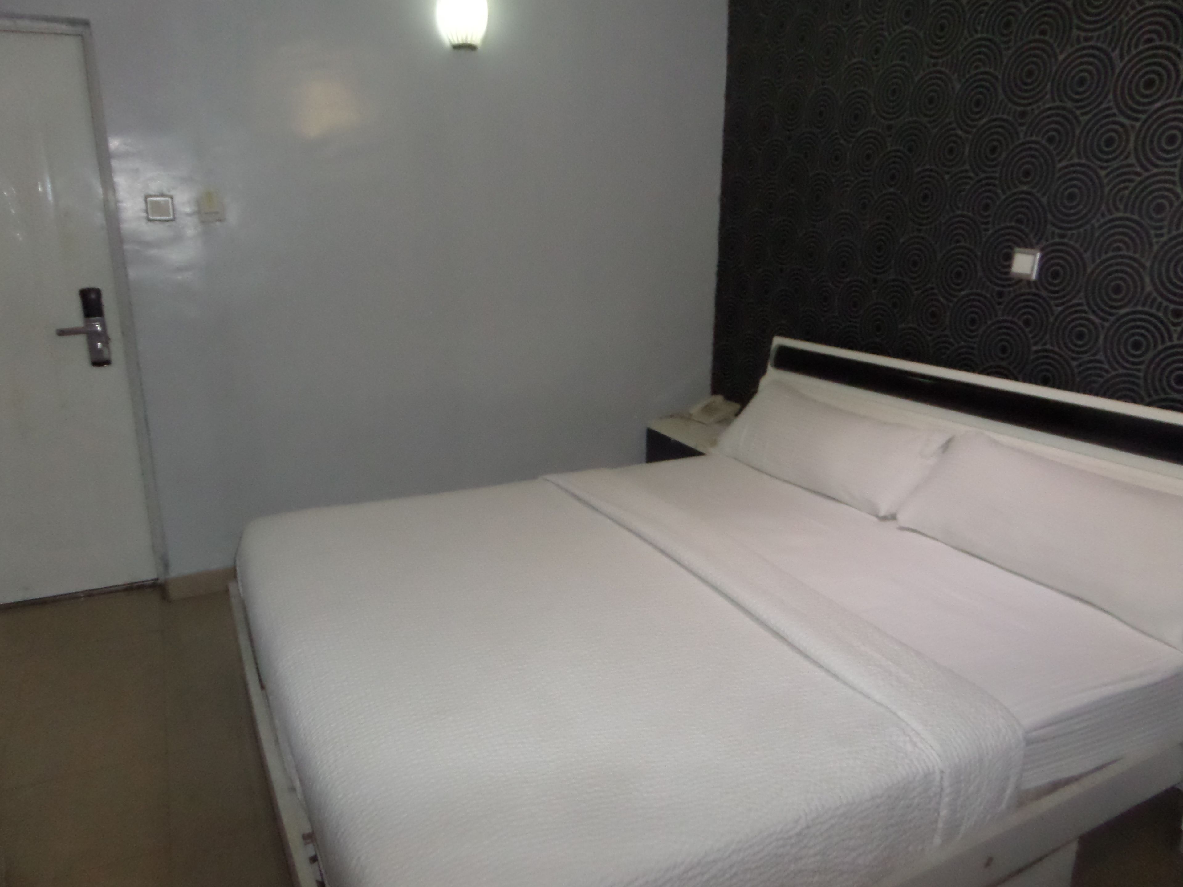 A single bed with white bedding in a room with a patterned wall and a door.