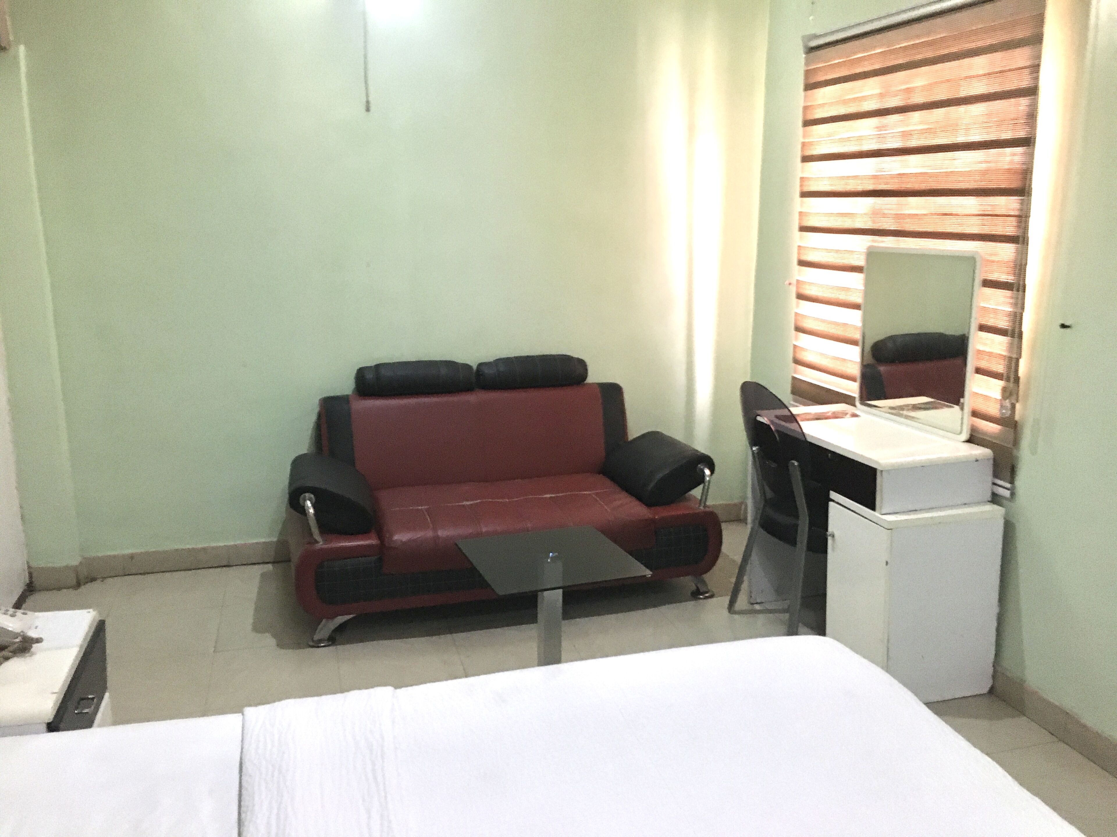 A compact hotel room with a single bed, a small desk, a chair, a sofa, and a mirror.
