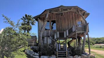 Une cabane en bois rustique, dotée d’un balcon et construite sur pilotis, entourée de rochers et de verdure.