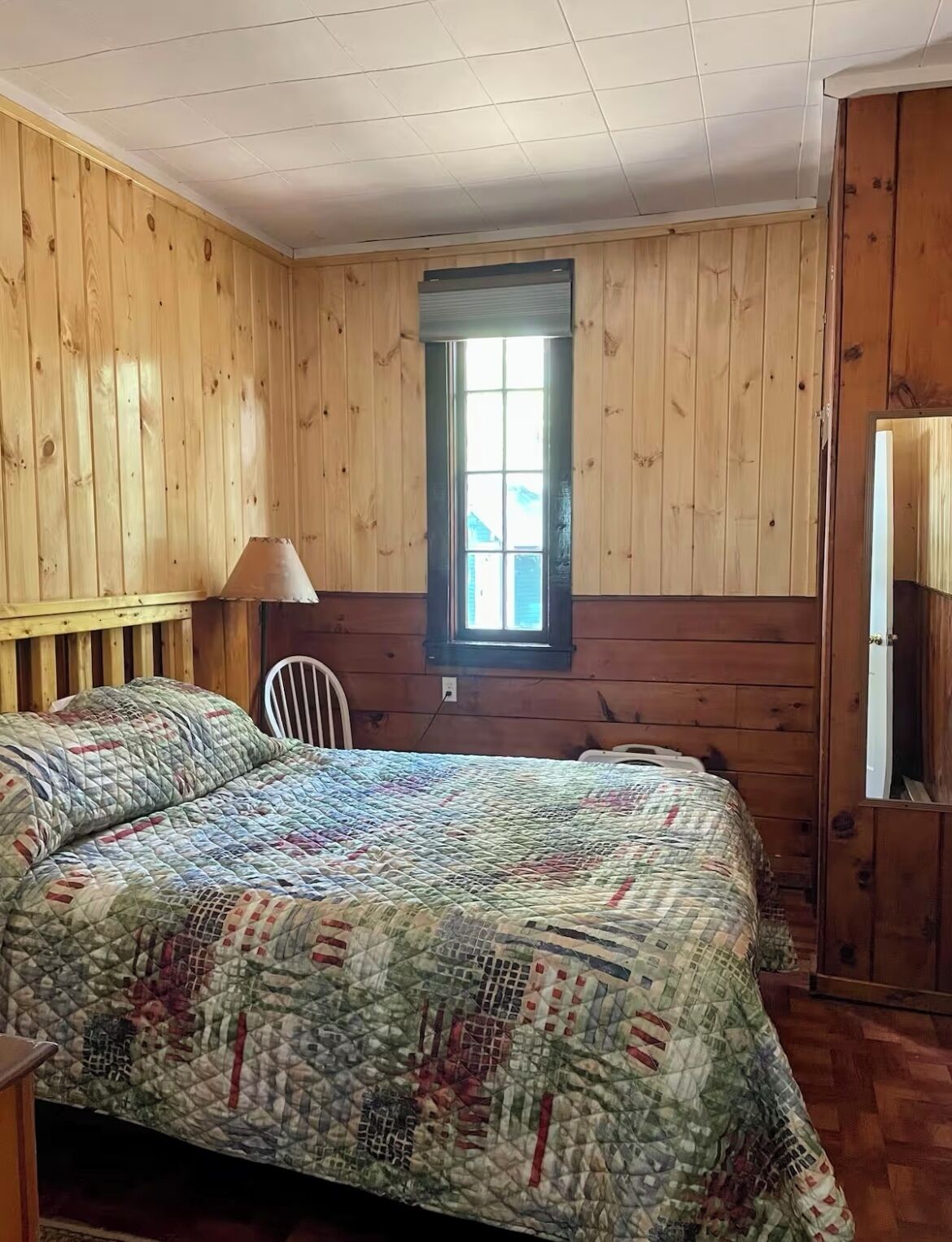 Een kamer met houten lambrisering, een bed, een stoel en een raam.
