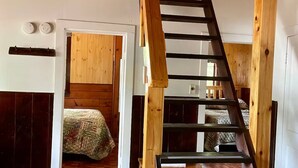 Una escalera de madera en una habitación con una cama y una puerta que da a otra estancia.