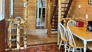Interior de una cabaña de madera con comedor, escalera y techo de madera.