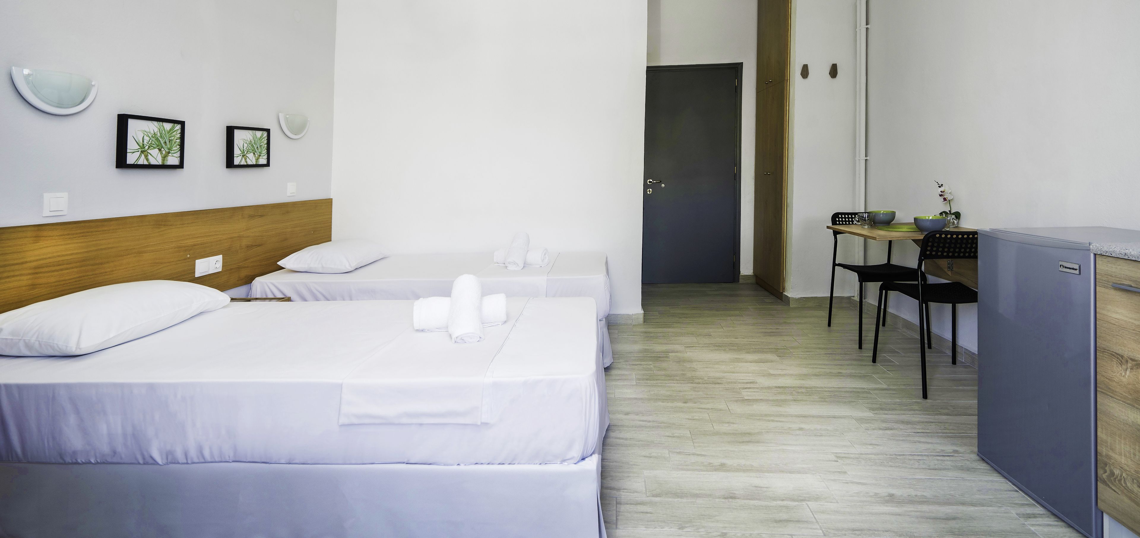 A hotel room with two beds, a desk, and a kitchenette.