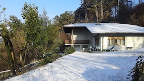 A house with a sloped roof, a covered porch, and a small deck with chairs. - B&B Marzola (Trento)