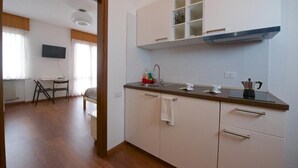 A modern kitchen with white cabinets, a countertop, and a built-in stove. There is a dining area with a table and chairs visible through an open doorway. - B&B Marzola (Trento)