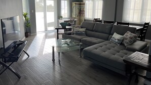Un salon spacieux avec un canapé gris, une table basse en verre et un téléviseur à écran plat.