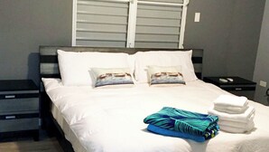 Un lit bien fait, avec des draps blancs, deux oreillers et une serviette bleue et verte pliée, posée sur le côté.