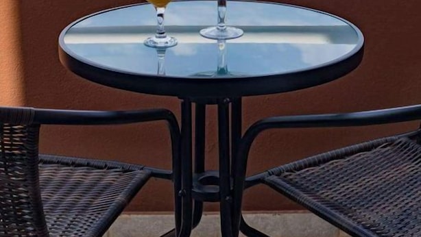 Ein runder Glastisch mit Orangensaft und einem abgedeckten Dessert auf einem Balkon mit Meerblick.