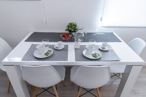 Mesa de jantar posta com cadeiras brancas, um jarro, uma tigela de morangos e uma pequena planta em vaso.