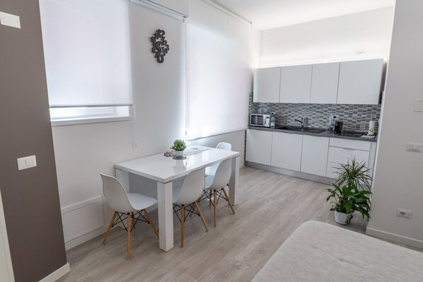 Cozinha moderna com armários brancos, micro-ondas e pia. Há uma mesa de jantar com cadeiras e um vaso de plantas.